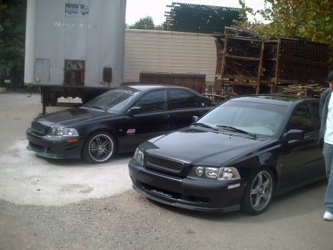 2006 Volkswagen GTI - Two black sedans are parked on a gravel lot with a large trailer and industrial debris in the background.