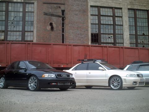 2006 Volkswagen GTI - Two sedans, a black Audi A4 and a white Audi A4, are parked outdoors in front of a train car and industrial building.