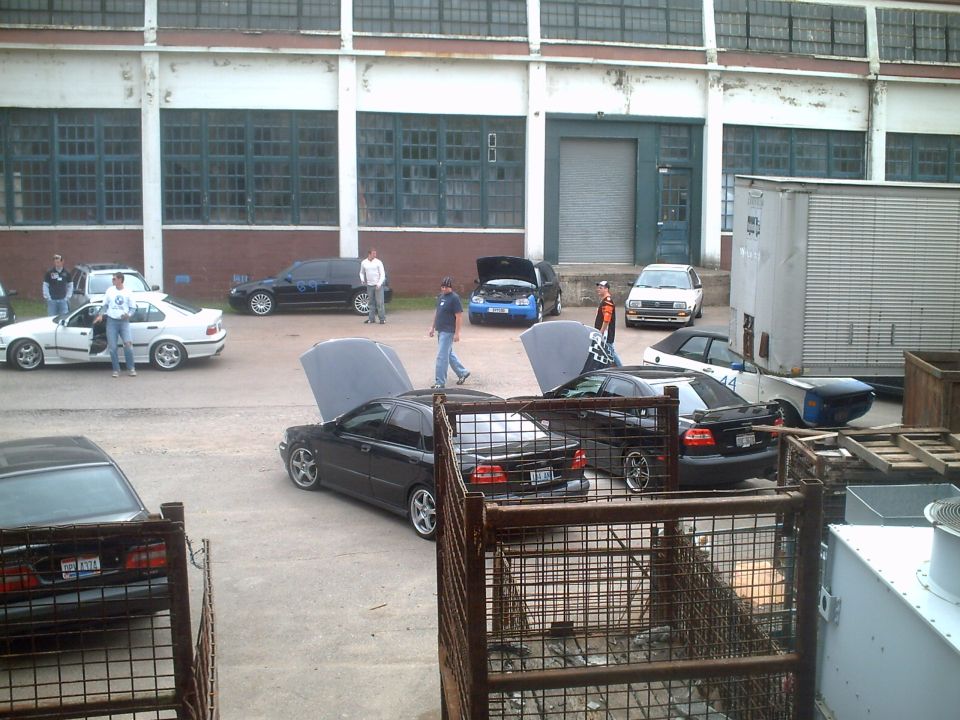 Several cars are parked outside a warehouse, some with hoods open. The 2006 Volkswagen GTI is visible