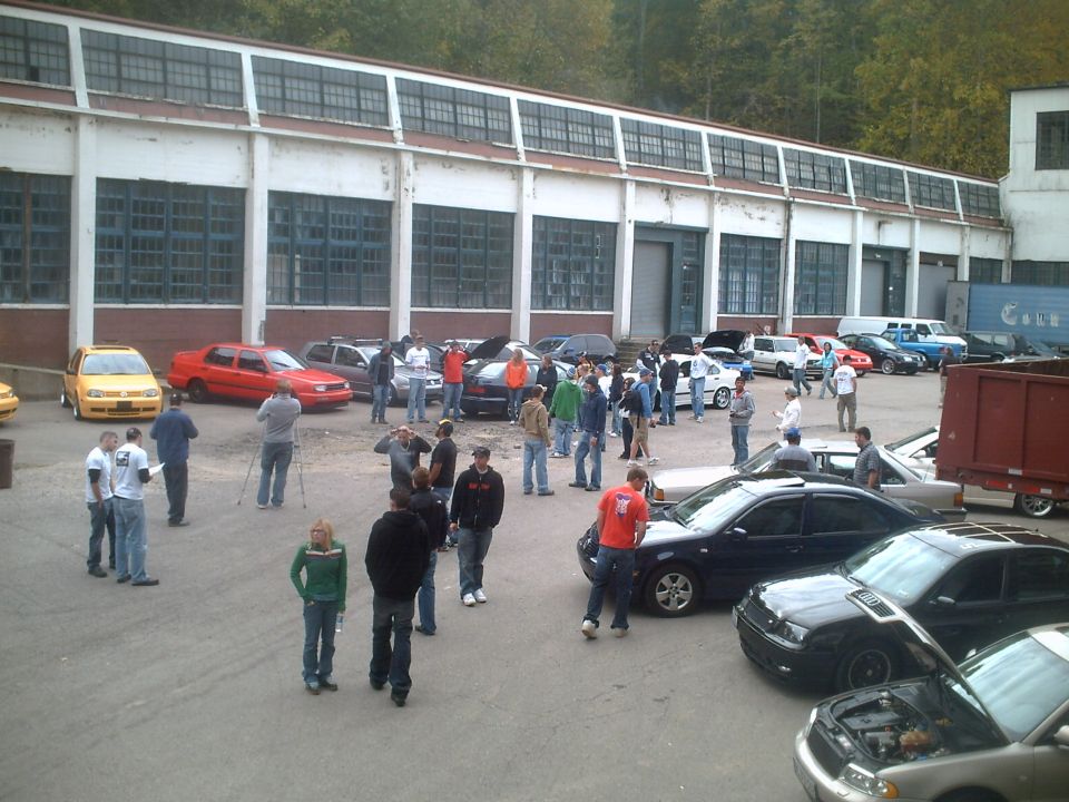Cars and people gathered in a lot outside a large industrial building