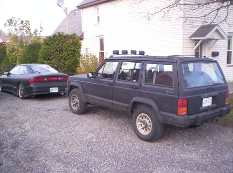 1990 Jeep Cherokee - A black 1990 Jeep Cherokee is parked next to a black coupe.
