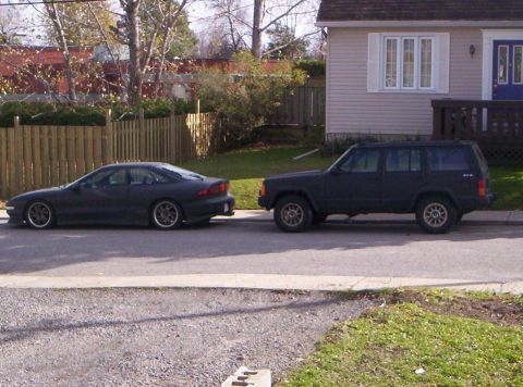 1990 Jeep Cherokee - A 1990 Jeep Cherokee and a dark sedan are parked on the side of a street in front of a house.
