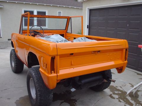 1977 Ford Bronco - This orange Ford Bronco is missing its doors and top, parked in front of a garage.