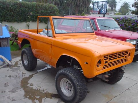 1977 Ford Bronco - This orange 1977 Ford Bronco is parked in a driveway next to a red Ford truck.