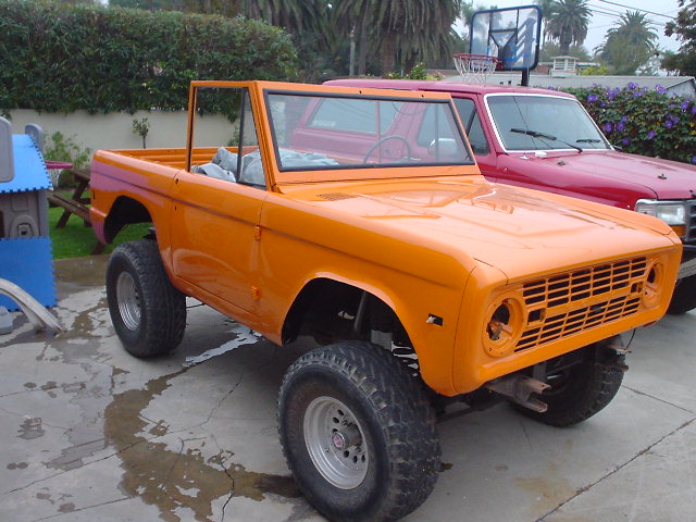 Orange 1977 Ford Bronco with a red Ford truck behind it