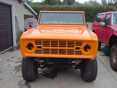 1977 Ford Bronco - Front view of an orange 1977 Ford Bronco undergoing restoration, with a red SUV visible to the right.