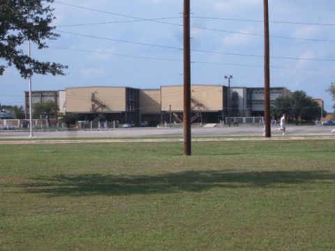 1988 Ford Bronco - A white SUV is visible in the distance, parked in front of a large, tan building under a cloudy sky.