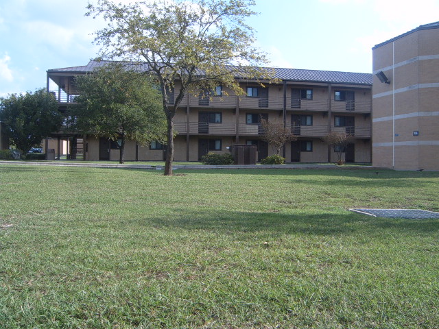 Building with balconies and trees in front of a grassy field