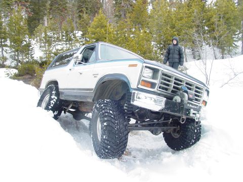 1986 Ford Bronco - A lifted Ford Bronco navigates a snowy incline with a person standing on the hood.