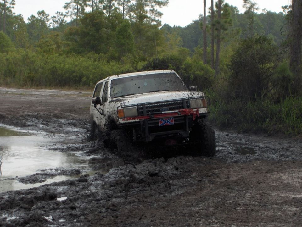 1989 Ford Bronco stuck in thick mud on a dirt track, front bumper visible