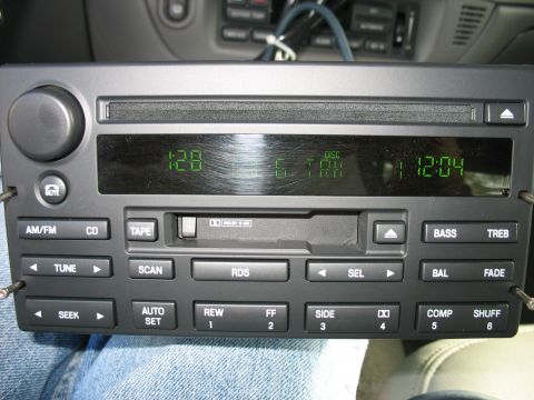 2003 Ford Crown Victoria - Car stereo unit with AM/FM, CD, and tape functions, a digital display and numerous buttons.