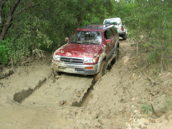 Red 1996 Toyota 4Runner navigating a muddy trail with another white SUV behind it