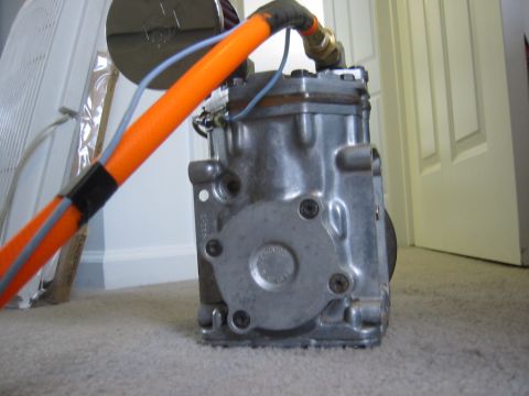 1995 Ford Bronco - Close-up of an air conditioning compressor with attached hoses and wires, resting on a carpeted floor.