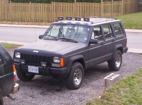 1990 Jeep Cherokee - This 1990 Jeep Cherokee SUV is parked on a gravel surface with a wooden fence in the background.