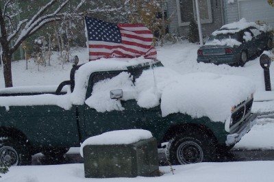 1972 Ford Ranchero - A green pickup truck is covered in snow, with an American flag displayed on its roof.