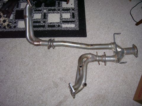 1993 Mazda MX-6 - Two sections of exhaust piping, likely from a vehicle, are laid out on a carpeted floor.