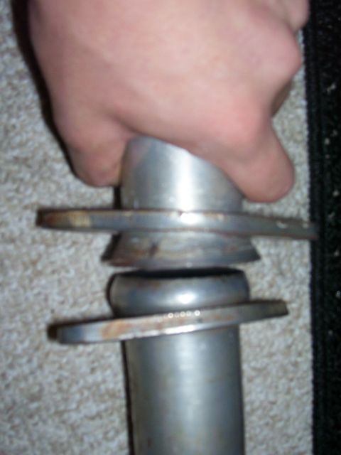 1993 Mazda MX-6 - A hand grips a metal exhaust pipe component, showing flanges and a flexible joint.