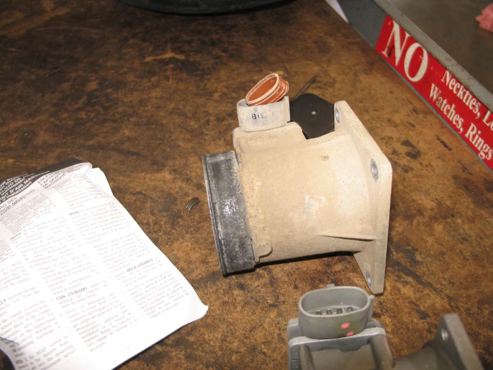 Mass air flow sensor with two gaskets and a wiring connector. Paper instructions are nearby