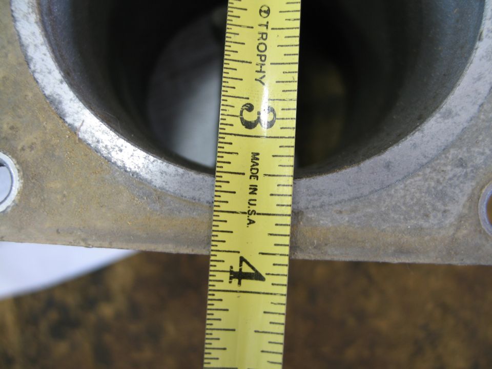 Tape measure across the twin bores of an aluminum intake casting on a rusty workbench
