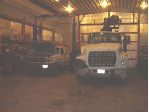 1992 Ford Bronco - Two trucks are parked inside a garage, one with its hood open and the other a large white truck.