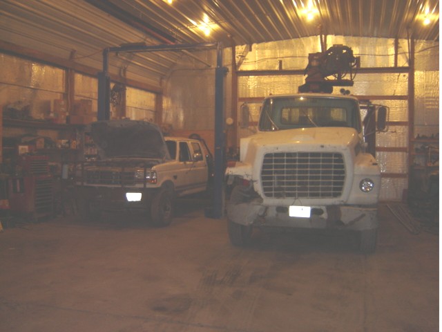 two trucks, one with hood up, inside a garage with a lift