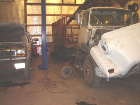 1992 Ford Bronco - A white SUV and a large white truck with a crane are parked inside a garage, with a vehicle lift visible.