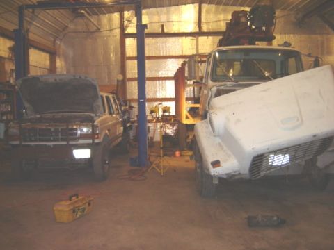 1992 Ford Bronco - Two vehicles, a 1992 Ford Bronco and a white truck, are in a garage with one on a lift.