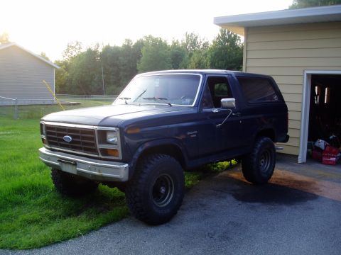 1986 Ford Bronco - A dark blue Ford Bronco is parked on a driveway next to a garage on a sunny day.