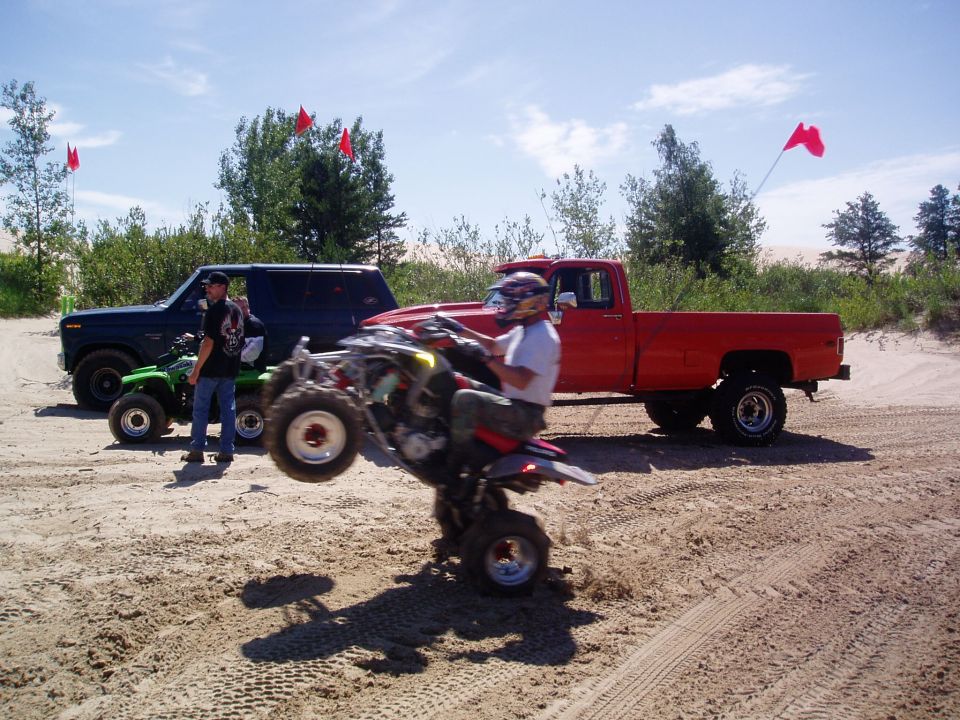Red pickup truck and blue SUV with ATVs on sandy terrain