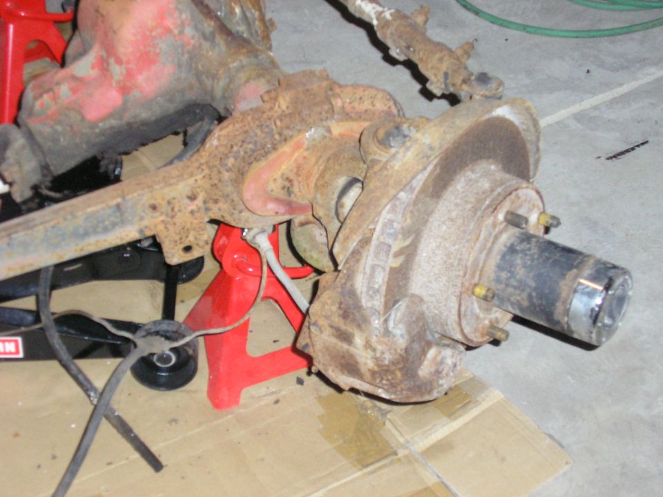 Rusty front axle assembly with brake rotor and hub on a jack stand in a garage