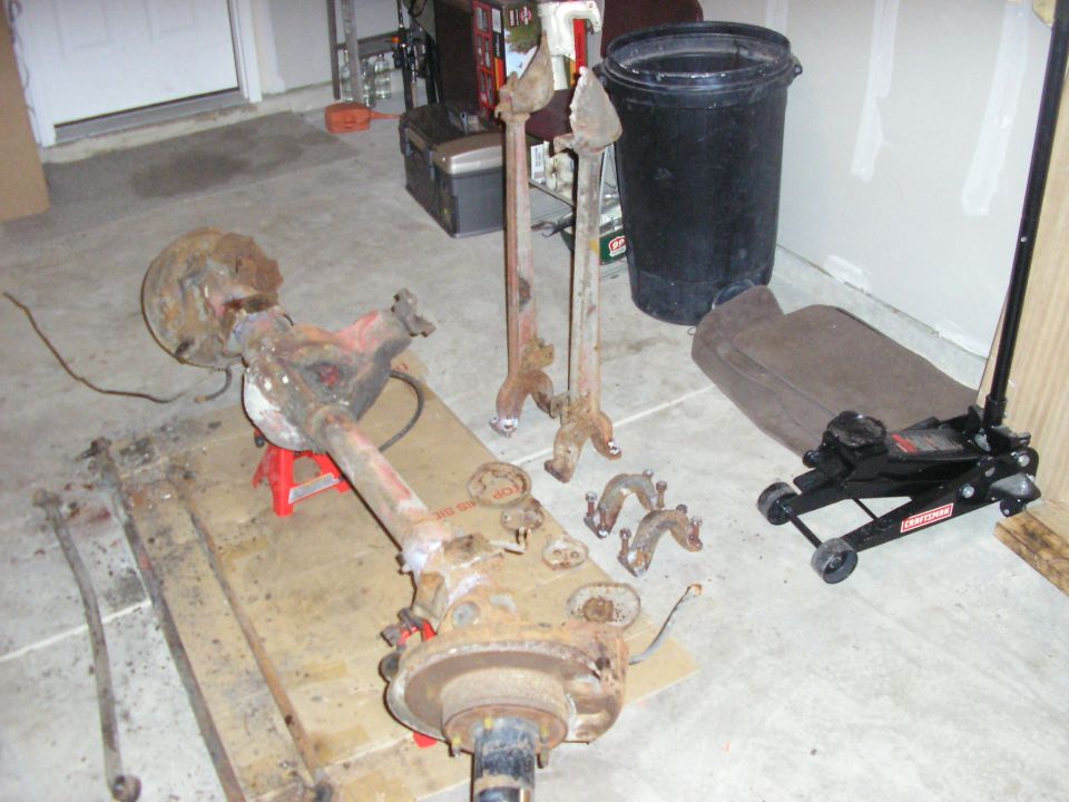 Rusty rear axle assembly on red jack stands with a floor jack and other parts