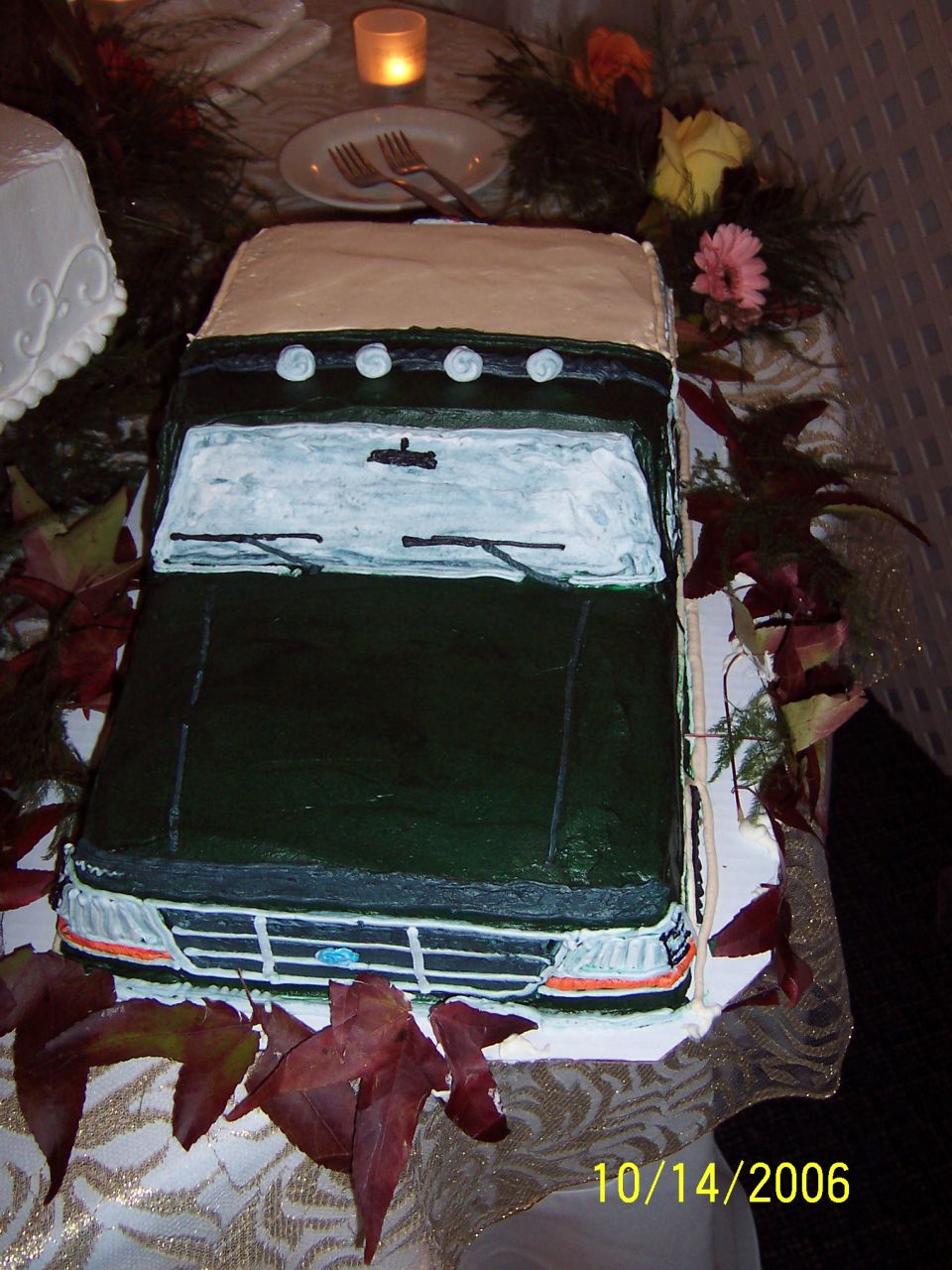 Green SUV-shaped cake with tan roof, viewed from front, on a decorated table