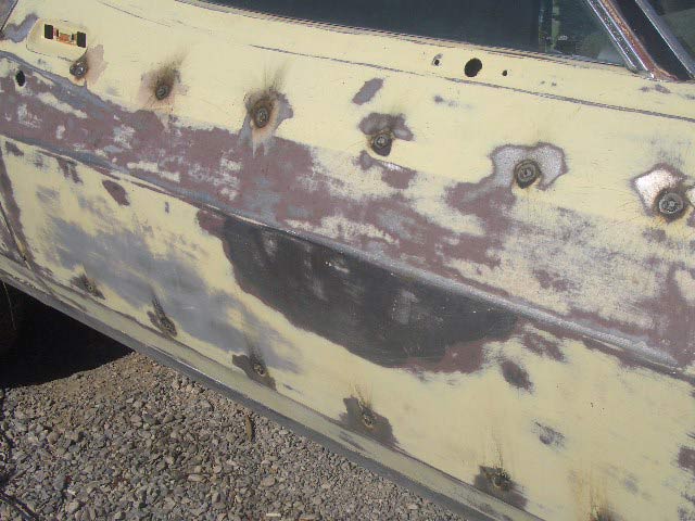 Door panel of a car stripped to bare metal and primer with bolt holes