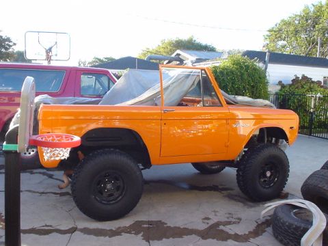 1977 Ford Bronco - Orange 1977 Ford Bronco with a basketball hoop mounted on the front, parked next to another vehicle.