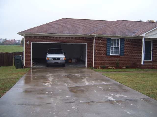 White van parked in an open garage, wet driveway in foreground