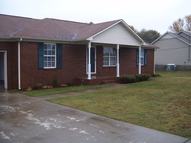 Brick house with a covered porch and shutters. Lawn and driveway in front