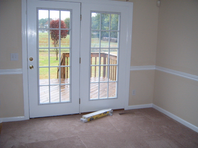 Interior room with beige walls, carpet, and white french doors opening to a wooden deck and yard