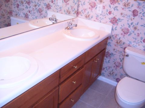 1988 Ford Bronco - A bathroom scene a double vanity with white sinks, wooden cabinets, and floral wallpaper, adjacent to a toilet.