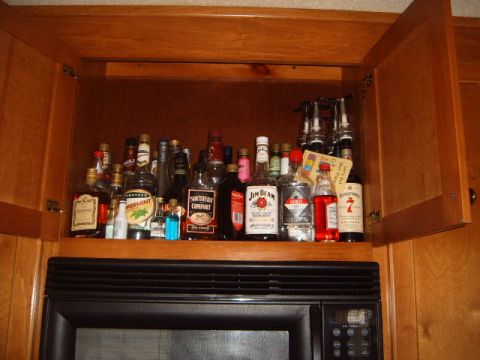 1988 Ford Bronco - A collection of various liquor bottles are stored on shelves within a wooden cabinet.
