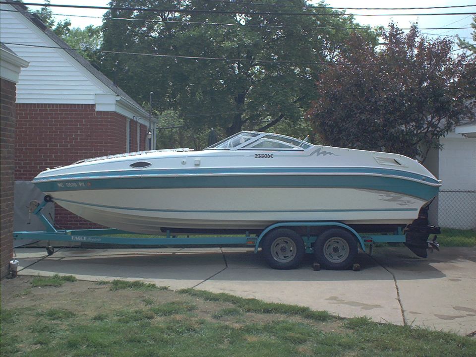 Teal and white powerboat on a tandem-axle trailer parked in a driveway by brick houses