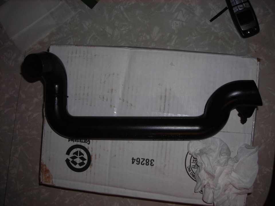 Black metal automotive pipe on a cardboard box, with a cell phone in the background