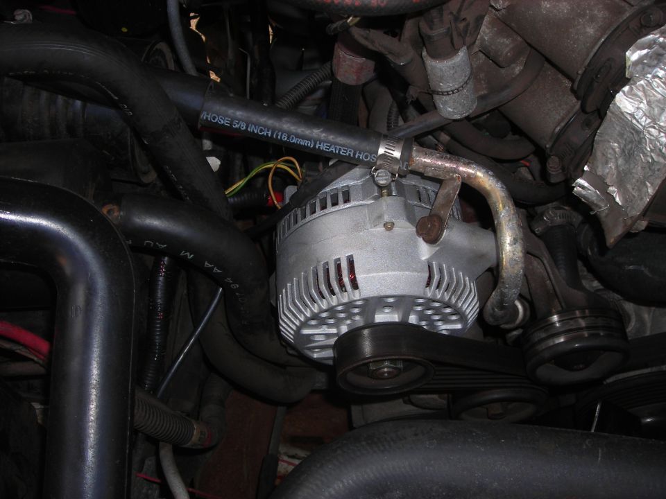 Alternator with ribbed belt and heater hose in engine bay