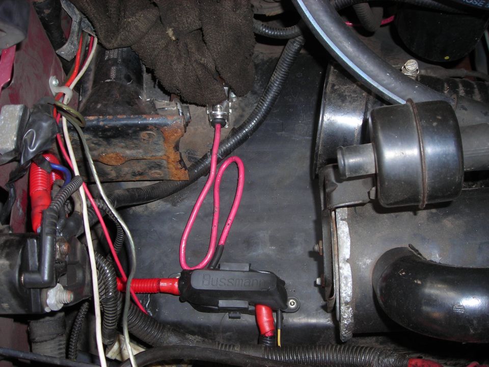 Close-up of engine bay wiring with a Bussmann fuse holder and red wires
