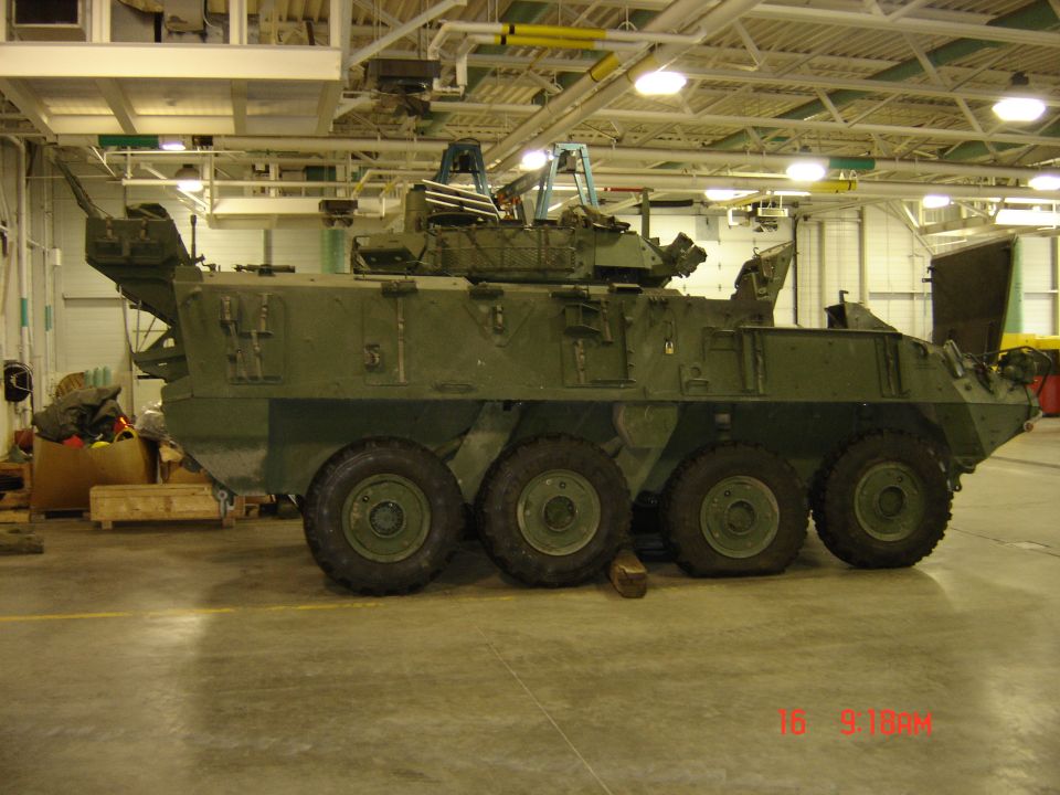 Green military armored vehicle with six wheels parked indoors