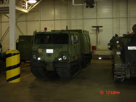 1990 Ford Bronco - A military tracked vehicle is parked indoors, with another vehicle visible to its right.