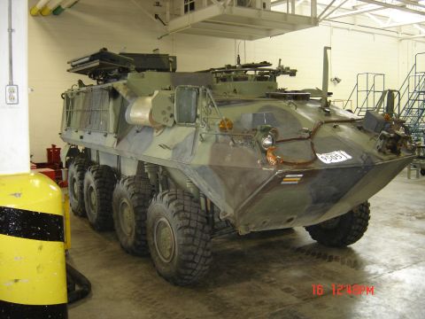 1990 Ford Bronco - An eight-wheeled armored personnel carrier with camouflage paint is parked inside a building.