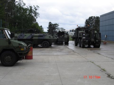 1990 Ford Bronco - A collection of military vehicles, including armored personnel carriers and trucks, are parked outdoors on a cloudy day.