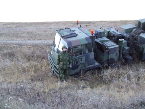 1990 Ford Bronco - A military truck with camouflage paint is parked in a grassy field next to a person in uniform.