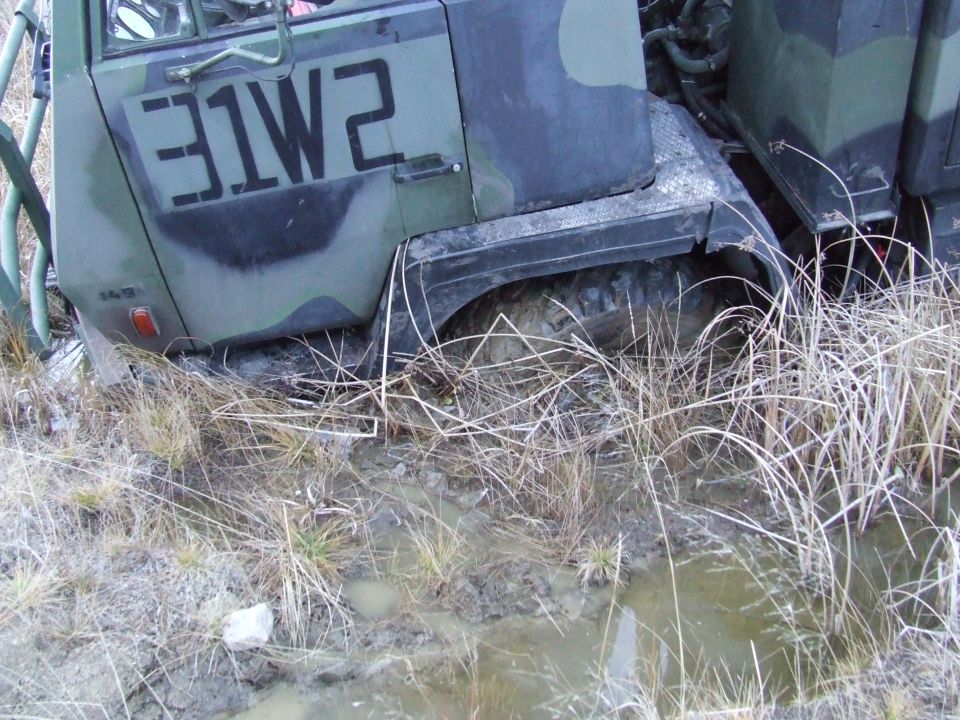 Green military truck with black markings stuck in muddy terrain
