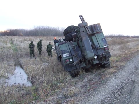 1990 Ford Bronco - Military truck stuck in a ditch with soldiers observing the situation.